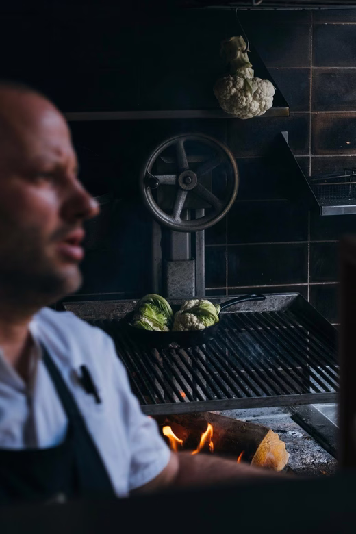 Chef in apron near grill with cauliflower and lettuce cooking over fire