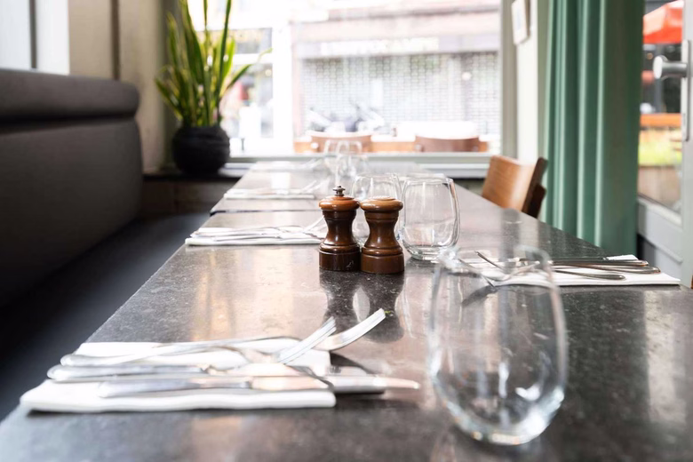 Dining table set with cutlery, glasses, and salt and pepper shakers in a restaurant.
