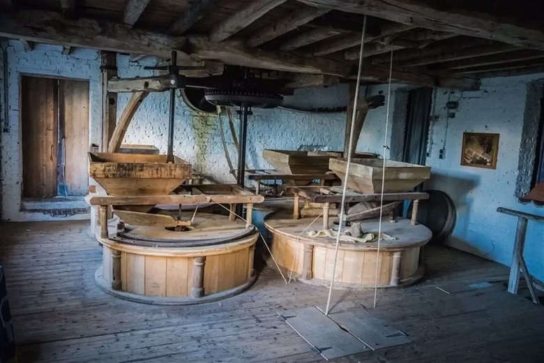 Interior of an old wooden grain mill with grinding stones and a wooden swing.