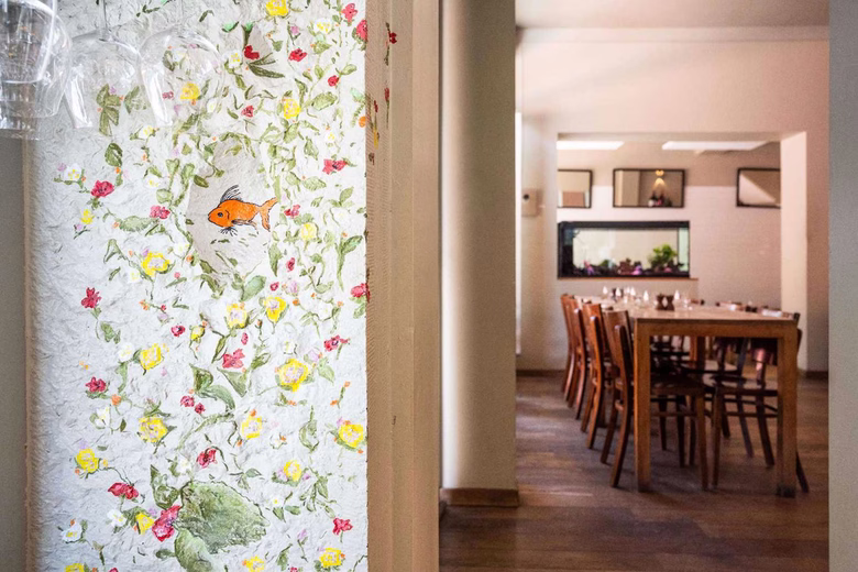 Wall with floral mural and goldfish next to a dining room with wooden table and chairs
