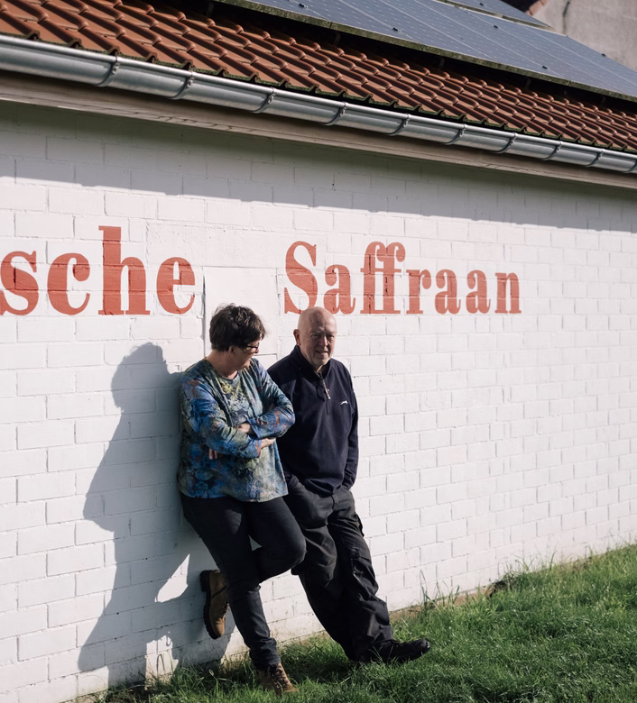Two people leaning against a white brick wall with red text, under a roof with solar panels.