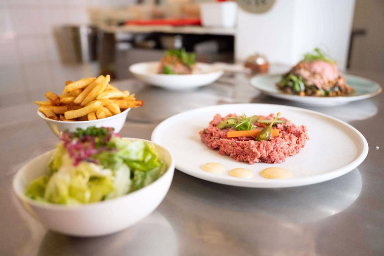 Plate of steak tartare with sauces, bowl of fries, and bowl of salad on a table