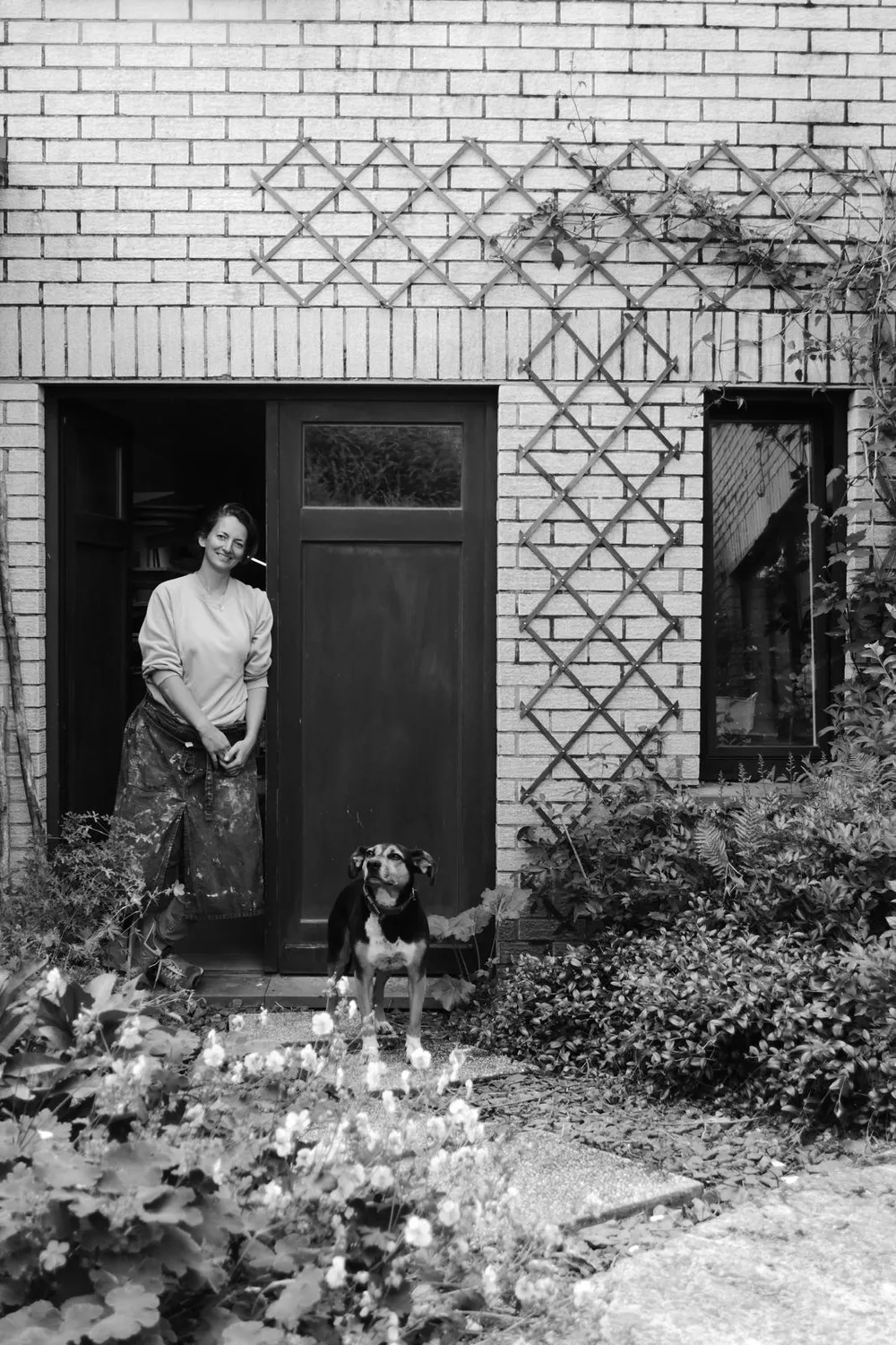 Eva Kengen e tablier devant la porte d'entrée de l'atelier avec le chien Tokyo